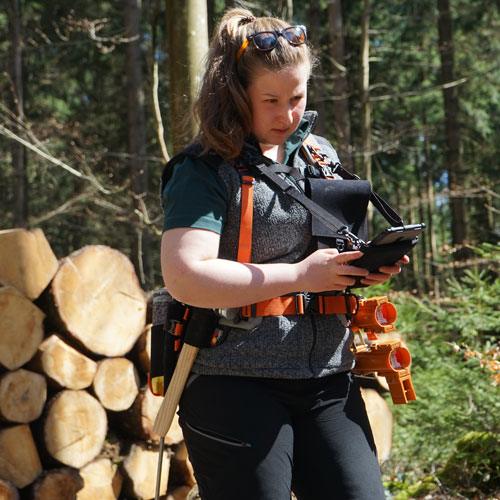 Försterin mit Förster Forstgürtel, Schultertragesystem und Baukasten-Modulen bei der Arbeit mit einem Tablet im Wald.