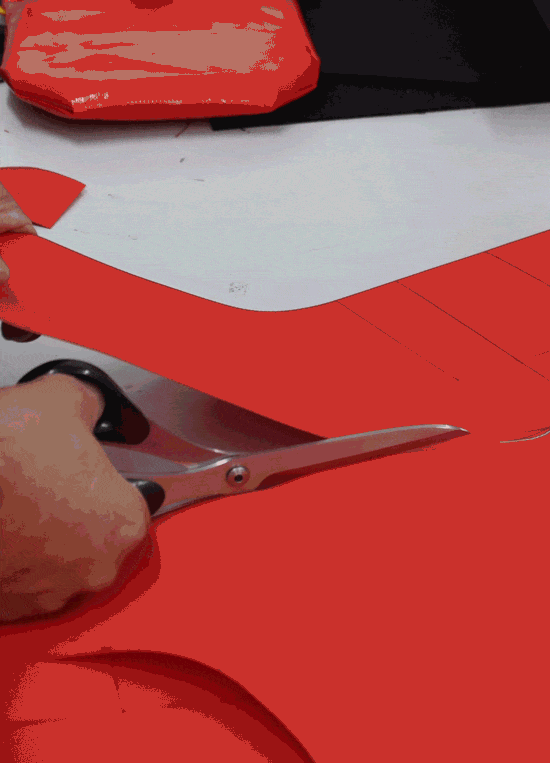 Nahaufnahme eines Handwerkers, der roten Stoff für die Herstellung von Fuegos Pflanztaschen mit einer Schere zuschneidet.